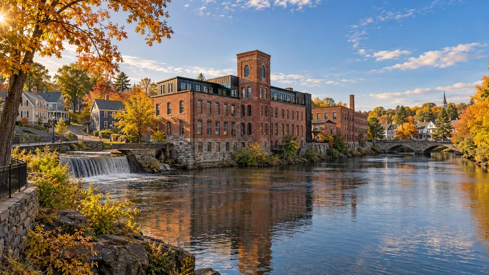 Red-brick mill beside a river, stone bridge and autumn trees in a West Warwick-inspired setting